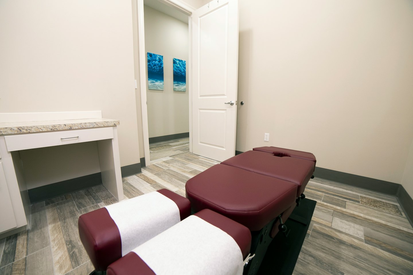 Modern medical room with maroon treatment table and white desk.