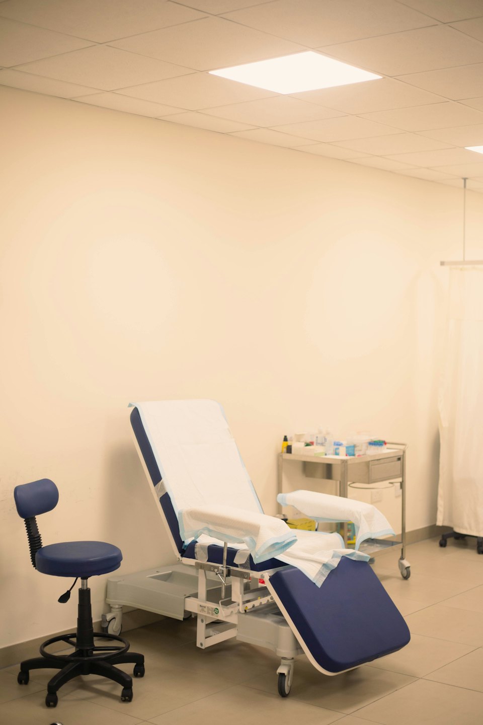 Empty medical examination room with blue and white chair and cart.
