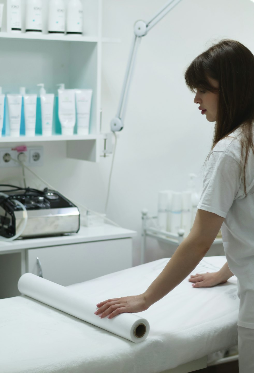 An aesthetician unrolls white paper onto a spa treatment bed.